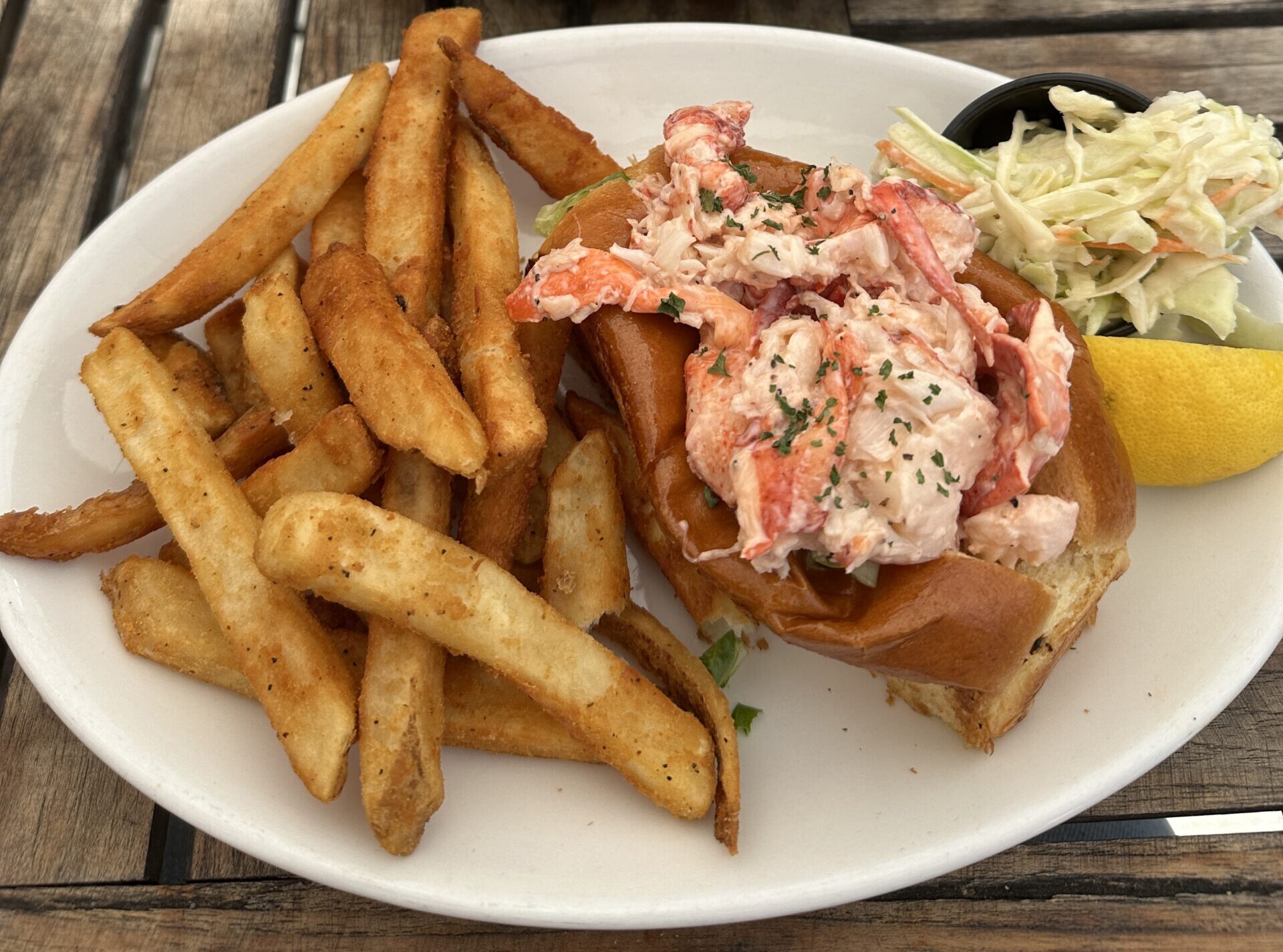 a closeup of a New England lobster roll sandwich served with fries