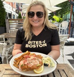 A blonde woman in a black shirt with a plate that has a lobster roll