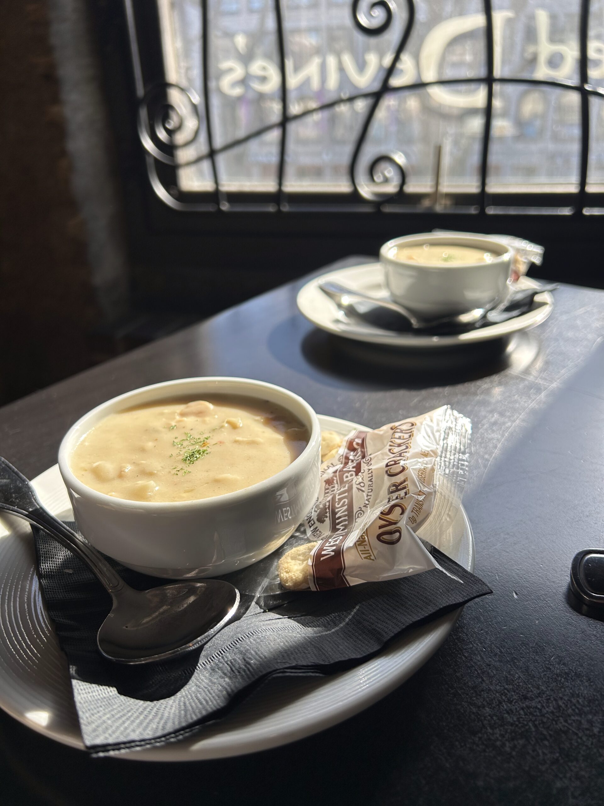 A bowl of clam chowder with a packet of oyster crackers alongside