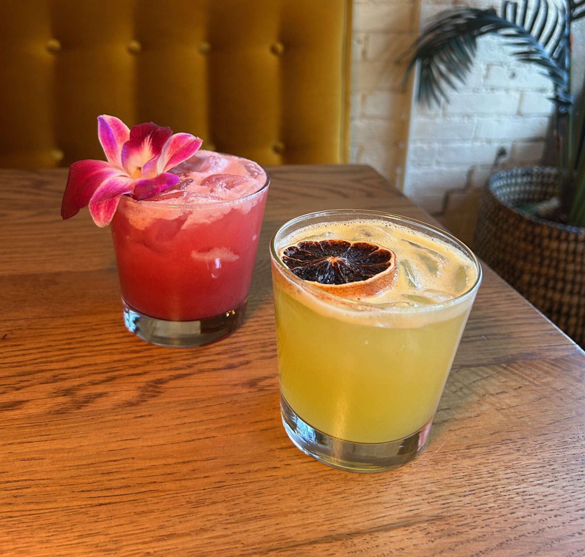 Two cocktails on a wooden bar, one topped with a pink orchid